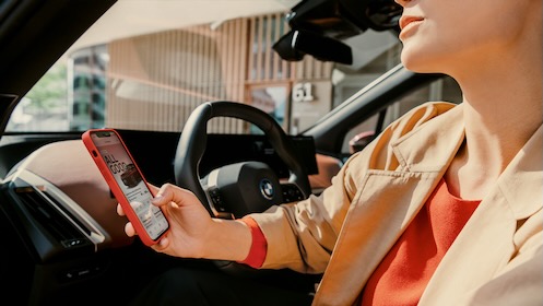 Woman holding smartphone standing in front of a BMW car